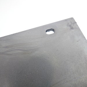 K&ouml;nnte beinhalten: Nahaufnahme einer grauen Metallplatte mit einem kleinen Loch in der Mitte. Die Platte hat eine strukturierte Oberfl&auml;che und scheint leicht verkratzt zu sein.