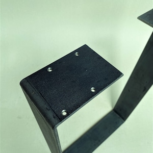 May include: Black metal table legs with a square design and rounded edges. The legs have multiple holes drilled into the top surface.