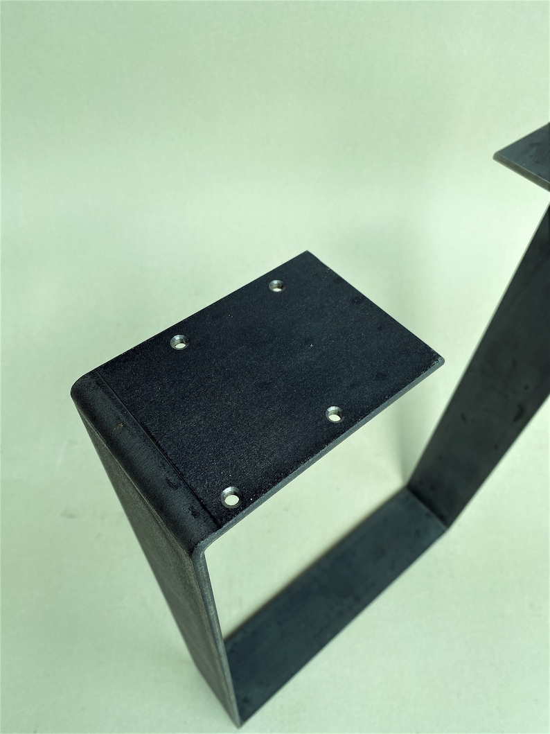 May include: Black metal table legs with a square design and rounded edges. The legs have multiple holes drilled into the top surface.