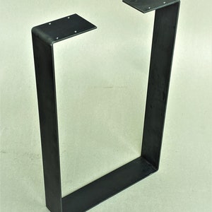 May include: Black metal table leg with a rectangular shape and a welded seam. The leg is made of thick metal and has a simple, industrial design.