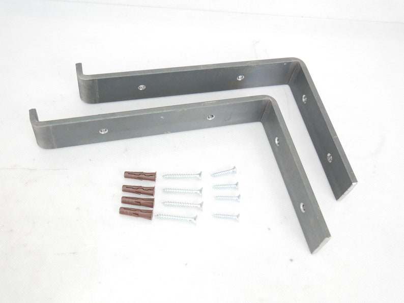 Puede incluir: Dos soportes de estante de metal con cuatro tornillos de montaje y cuatro tacos de pl&aacute;stico. Los soportes son de color gris oscuro y tienen una forma ligeramente curvada.