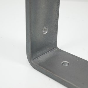 K&ouml;nnte beinhalten: Nahaufnahme einer Metallhalterung mit zwei vorgebohrten L&ouml;chern. Die Halterung ist hellgrau und hat eine leicht strukturierte Oberfl&auml;che.