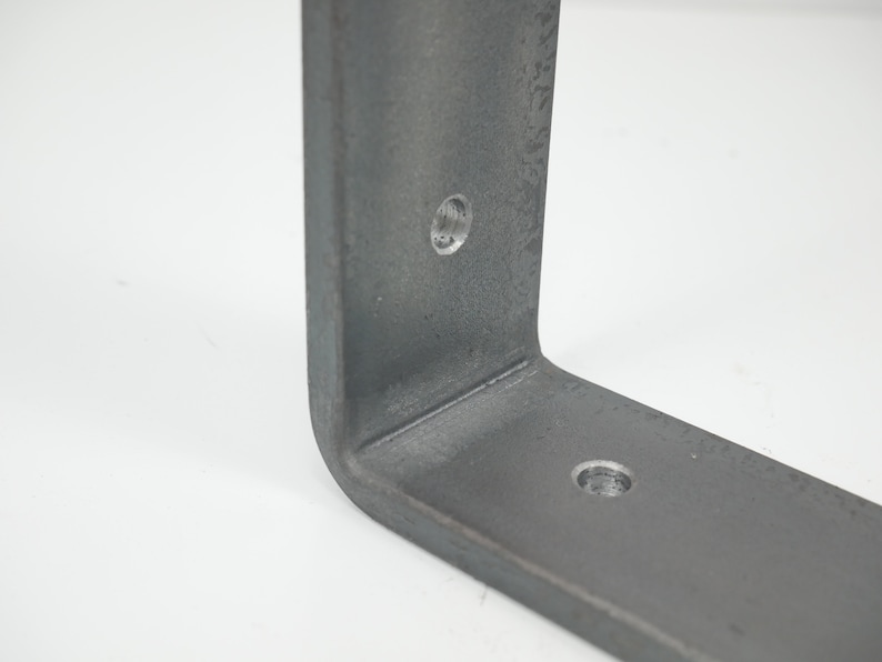 K&ouml;nnte beinhalten: Nahaufnahme einer Metallhalterung mit zwei vorgebohrten L&ouml;chern. Die Halterung ist hellgrau und hat eine leicht strukturierte Oberfl&auml;che.