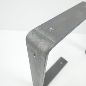 K&ouml;nnte beinhalten: Ein Paar Tischbeine aus Metall mit grauer Oberfl&auml;che. Die Beine sind L-f&ouml;rmig und haben eine abgerundete Ecke. In jedes Bein sind drei L&ouml;cher gebohrt.