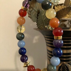 May include: A rainbow colored beaded bracelet with gold accents. The bracelet is made of various gemstones, including amethyst, lapis lazuli, and clear quartz.
