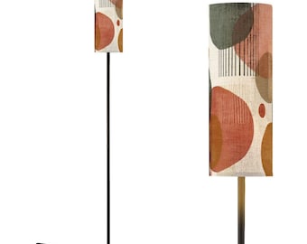 May include: A tall, black floor lamp with a cylindrical lampshade. The lampshade features a cream-colored background with abstract shapes in shades of orange, brown, and green. The lamp has a round base and a foot switch.
