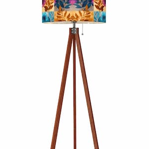 May include: A wooden tripod floor lamp with a patterned lampshade. The shade features a patchwork design with floral and leaf motifs in shades of blue, gold, and purple. The lamp has a pull chain.