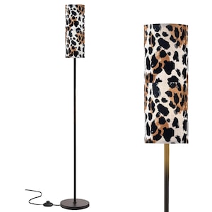 May include: A floor lamp with a cylindrical lampshade featuring a leopard print pattern in black, brown, and cream. The lamp has a dark metal pole and a round base. The lamp is plugged into an electrical outlet.