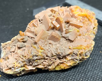 Könnte beinhalten: Ein Cluster aus orangefarbenen und gelben Barytkristallen auf einer grauen Matrix. Die Kristalle sind scharf und gut definiert, mit einem glasartigen Glanz.