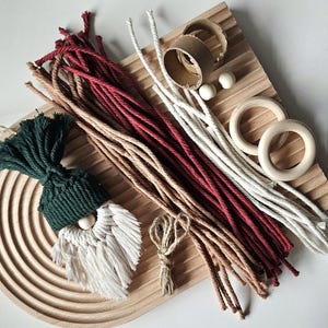 May include: A collection of craft supplies on a wooden tray. Includes red, white, and tan cords, wooden rings, small wooden beads, and a gnome ornament with a green hat and white beard. Perfect for DIY projects.