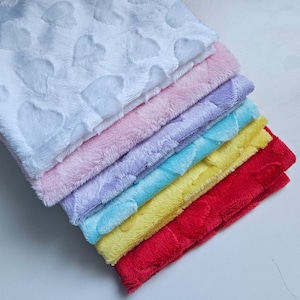 May include: A stack of seven plush fabric squares with a heart pattern. The squares are in different colors, including white, pink, lavender, light blue, yellow, and red.