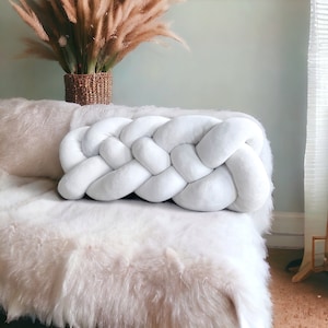 May include: White braided pillow with a soft, fluffy texture. The pillow is made of a thick, woven fabric and is perfect for adding a touch of comfort and style to any room.