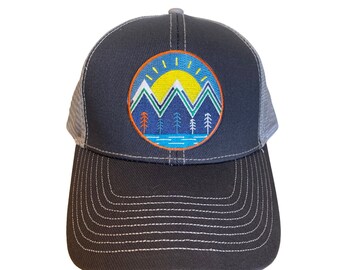 May include: A black and gray trucker hat with a blue, green, yellow, and orange embroidered patch of a mountain range with a sun and trees.