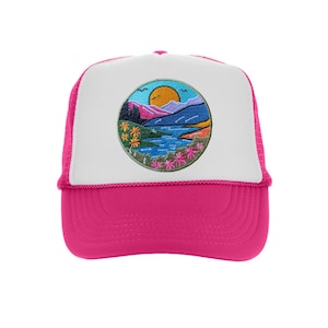 Pode incluir: Boné de caminhoneiro rosa choque com painel frontal branco. O chapéu apresenta um patch circular bordado que mostra uma paisagem com montanhas, um lago e um sol poente. Possui uma parte traseira em malha e uma viseira curva.