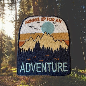 May include: Embroidered patch with a blue background, featuring a mountain range, a full moon, and the text "Always Up For An Adventure".