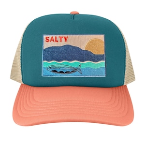 May include: A teal and coral trucker hat with a mesh back. The front panel features an embroidered patch with the word "SALTY" above a coastal scene with a fish, waves, and a sun.