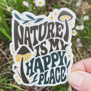 May include: A white sticker with the text "Nature is my happy place" in brown and green lettering. The sticker features a stylized mushroom with a yellow cap and brown stem.
