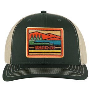 May include: A green and beige trucker hat with a patch featuring a mountain scene and the text "BRECK-CO".