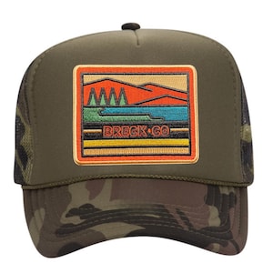 May include: A green camouflage trucker hat with a brown, orange, and yellow embroidered patch that says "BRECK CO" and depicts a mountain scene with a lake.
