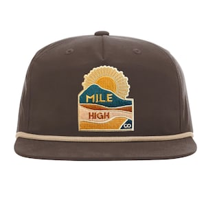 May include: A dark brown five-panel cap featuring a beige rope detail across the base of the crown. An embroidered patch on the front displays a yellow sun rising over teal and tan mountains with the text MILE HIGH CO in dark blue and brown.