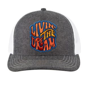 May include: A gray and white trucker hat with a colorful embroidered patch that says "Livin' the Dream".