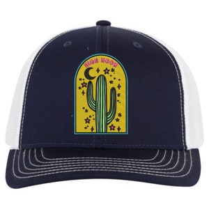 May include: A navy blue and white trucker hat with a yellow, green, and pink embroidered patch that says "High Noon" and features a cactus and stars.