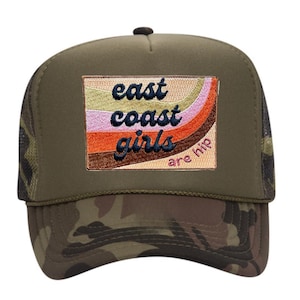 May include: Olive green trucker hat with a camouflage brim. The hat features a rectangular patch with the words "east coast girls are hip" in a retro font and color scheme.