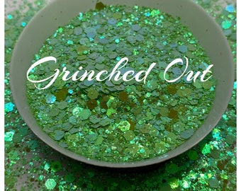 May include: A close-up of a bowl filled with green glitter with iridescent shimmer. The glitter is labeled "Grinched Out".