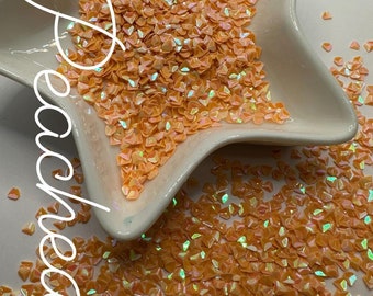 May include: Orange iridescent glitter in a star-shaped dish. The glitter is in the shape of small triangles. The text "$2 - .5 oz" is written on the image.