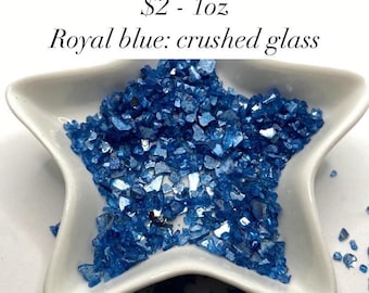 May include: A white star-shaped dish filled with crushed royal blue glass. The glass is iridescent and has a metallic sheen. The text "$2 - 1oz Royal blue: crushed glass" is visible above the dish.