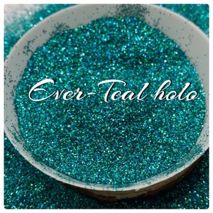 May include: A close-up of teal holographic glitter in a white bowl. The glitter has a shimmery, iridescent finish. The text "Ever-Teal holo" is written in cursive on the glitter.