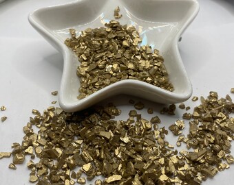 May include: A white ceramic star-shaped dish filled with gold glitter. The glitter is scattered around the dish on a white surface.