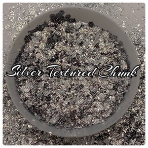 May include: A bowl filled with silver textured glitter chunks. The glitter is a mix of small and large pieces, with a variety of shapes and sizes. The glitter is a metallic silver color, with a slight iridescent sheen.