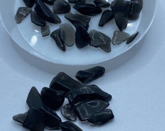 May include: Black glass chips in a white dish and scattered on a white surface. "Black glass chips" is written in black text at the top of the image.