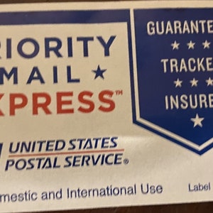 Puede incluir: Una etiqueta Priority Mail Express azul y blanca con el texto "GUARANTEED TRACKED INSURED" y el logotipo del Servicio Postal de los Estados Unidos. La etiqueta es para uso nacional e internacional.