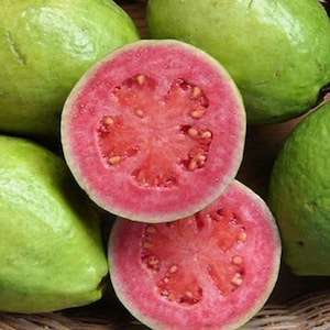 May include: A basket of whole and halved green guavas with pink flesh. The guavas are arranged in a wicker basket.