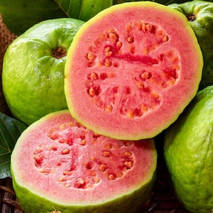 May include: Close-up of fresh guavas, some whole and some halved. The halved guavas reveal a vibrant pink interior with small, edible seeds. The outer skin is a light green color. The image showcases the fruit's texture and color.