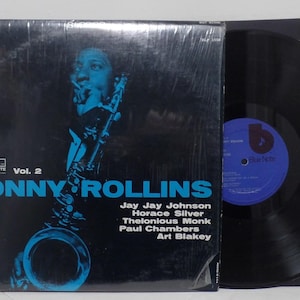 Puede incluir: Un álbum de vinilo vintage de Sonny Rollins, Vol. 2, con una portada azul y negra que presenta una ilustración de un saxofonista. El álbum incluye una lista de músicos y la etiqueta Blue Note.