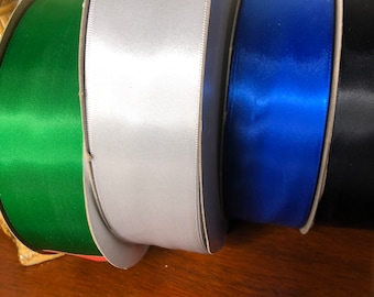 May include: Four rolls of satin ribbon in different colors: green, silver, blue, and black. The ribbon is wound around cardboard spools.