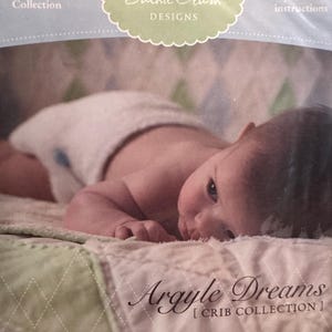 May include: A baby lying on a quilted crib bedding set with a green and white argyle pattern. The bedding set is part of the "Argyle Dreams" collection by Jackie Clark Designs. The text "4-Piece Collection" and "Easy-to-follow instructions" are visible on the packaging.