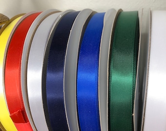 May include: A collection of spools of ribbon in various colors, including yellow, red, white, navy blue, royal blue, green, and white. The ribbon is wound around spools with a white cardboard center.