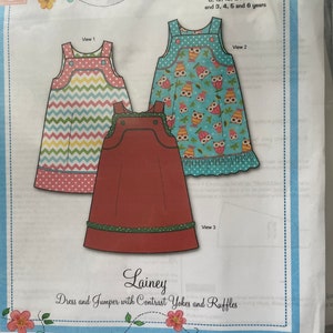 May include: A sewing pattern for a dress and jumper with contrast yokes and ruffles. The pattern includes sizes 6, 12, 18, and 24 months, as well as 3, 4, 5, and 6 years. The pattern features a red, green, and white jumper, a pink, yellow, and blue dress, and a blue dress with a colorful owl print.