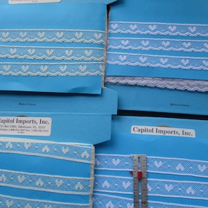 May include: Assortment of white lace trim with heart designs on blue card stock. The card stock has the text "Capitol Imports, Inc." and a phone number.