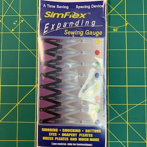 May include: A silver expanding sewing gauge with a black handle and a white label that reads "SimFlex Expanding Sewing Gauge". The label also includes the text "A Time Saving Spacing Device". The gauge is shown against a green grid background.
