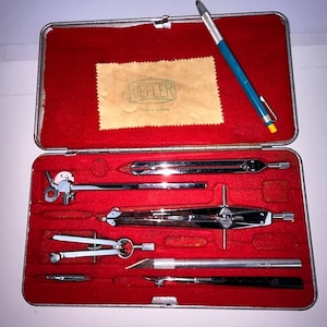 May include: A vintage drafting set in a metal case with a red velvet interior. The set includes various compasses, dividers, and a blue and silver pencil. A cleaning cloth with the "Riefler" logo is also included.