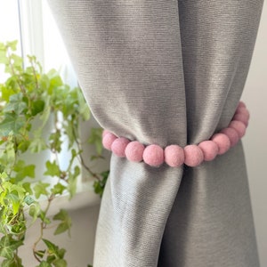 May include: A light grey curtain with a pink felt pom-pom tieback.