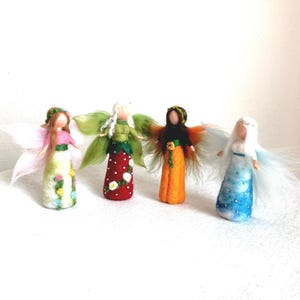 May include: Four handmade felt angel dolls with wings. Each doll has a unique design, including floral patterns, green and red dresses, and varying wing colors. The dolls are arranged on a white surface, showcasing their colorful details.