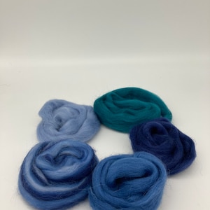 May include: Five balls of wool yarn in shades of blue and teal. The yarn is arranged in a circle on a white surface.