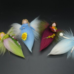 May include: Four handmade felt angel figurines with flowing hair and wings. Each angel has a unique colour scheme: green, blue, burgundy, and white. The angels hold various items, including a sunflower, a pumpkin, and a ball.