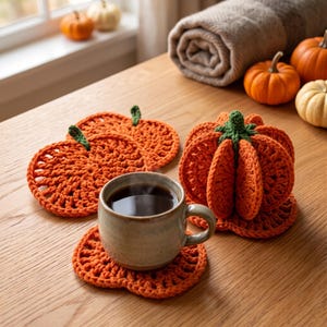 Peut inclure: Un ensemble de dessous de verre au crochet en forme de citrouille orange et une figurine de citrouille en crochet en trois dimensions. Un dessous de verre soutient une tasse en céramique remplie de liquide sombre. Fil orange texturé.